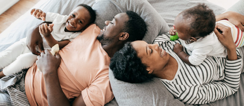 Aerial view of a mom, dad, and two young children on a bed smiling together before visiting their family dentist