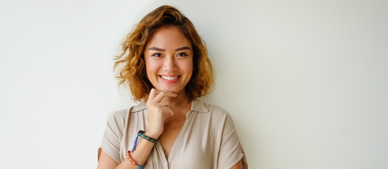 Brunette woman with dental implants smiles while wearing a beige shirt in Liberty, MO