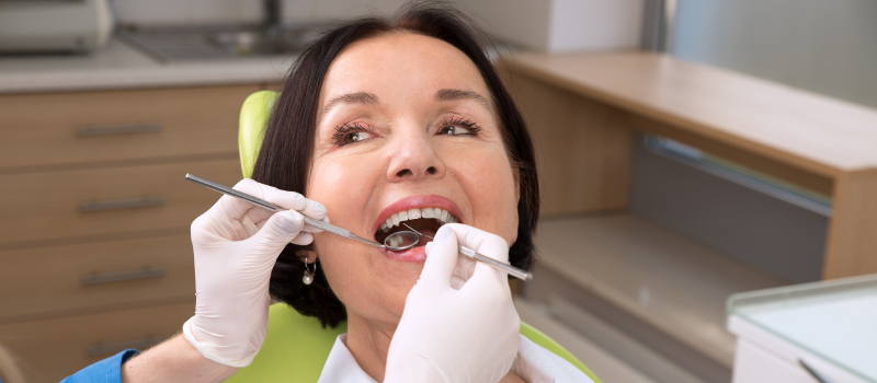 Brunette woman sits in a dental chair during a scaling and root planing procedure