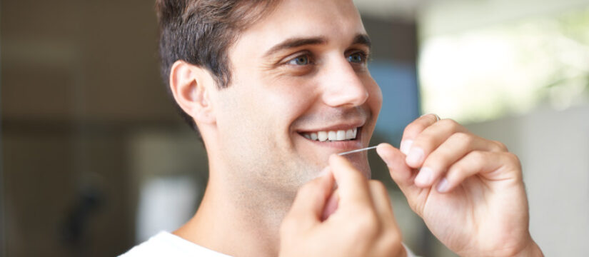 Brunette man smiles as he flosses between his teeth