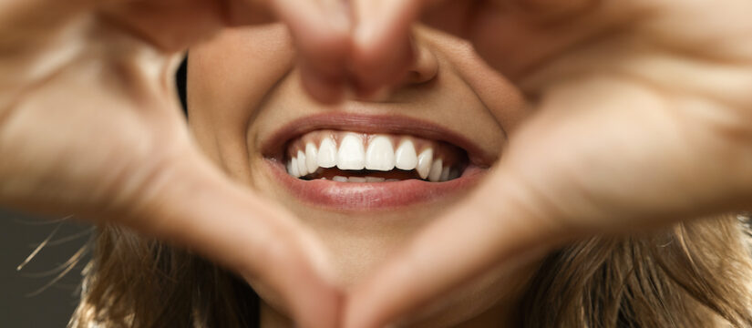 Closeup of a woman making heart hands around her beautiful smile after she receives treatment for teeth grinding