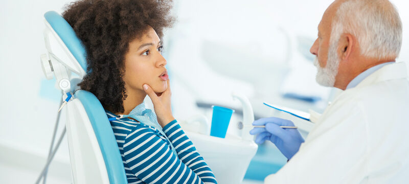 Black woman touches her cheeks and talks to her elderly dentist