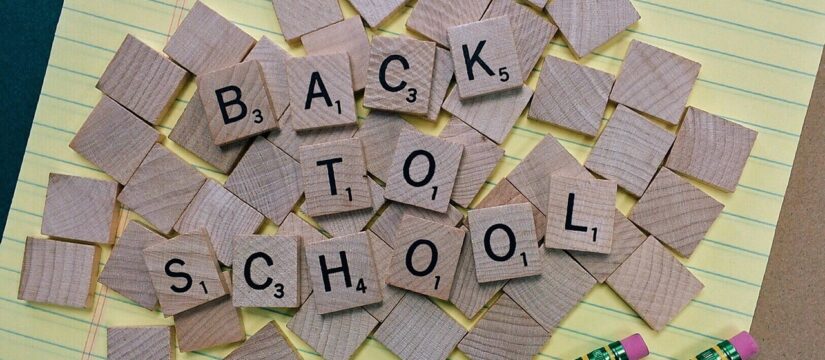 Aerial view of BACK TO SCHOOL on wooden Scrabble tiles on yellow notepad paper next to 2 yellow pencils