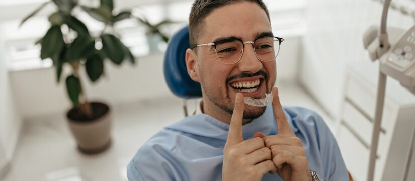 man in dental chair smiling with clear aligners, invisible braces